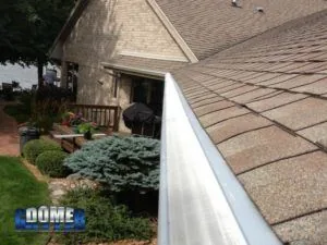 GutterDome guard along a roofline above patio shrubs.