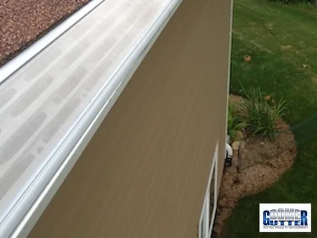 Asphalt shingle roof with GutterDome gutter guard — backyard run along brown siding.